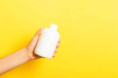 Kadın el tutarak krem şişe losyon izole. Kız sarı arka plan üzerinde tüp kozmetik ürünleri vermek