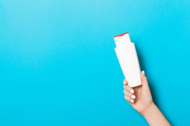 Kadın el tutarak krem şişe losyon izole. Kız mavi arka plan üzerinde tüp kozmetik ürünleri vermek