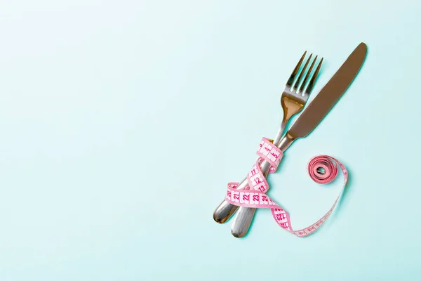 Crossed fork and knife are wrapped in measuring tape on blue background. Concept of diet for weight loss with copy space — Stock Photo, Image