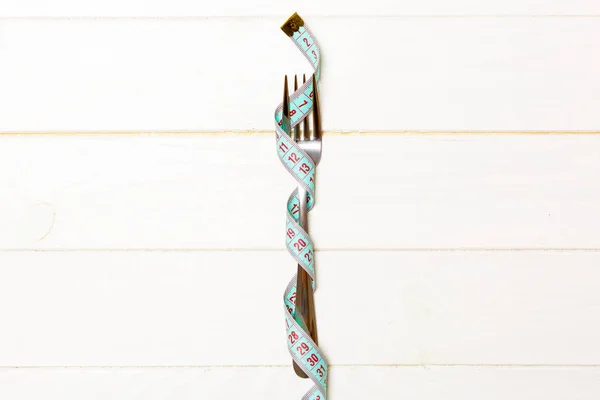 Diet concept with fork wrapped in measuring tape on wooden background. Top view of weight loss with empty space — Stock Photo, Image