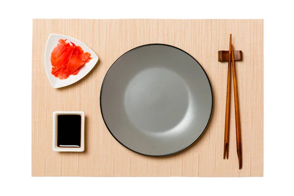 Placa gris redonda vacía con palillos para sushi y salsa de soja, jengibre sobre fondo de estera de sushi marrón. Vista superior con espacio de copia para su diseño — Foto de Stock