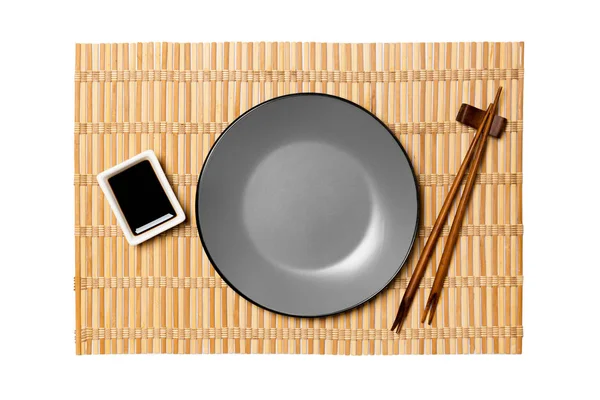 黄色い竹マットの背景に寿司と醤油のための箸と空の丸い灰色のプレート。デザイン用のコピースペース付きのトップビュー — ストック写真