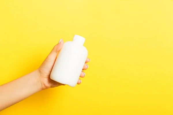 Botella de crema de mano femenina de loción aislada. Chica dar productos cosméticos tubo sobre fondo amarillo —  Fotos de Stock