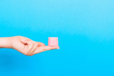 Kadın el tutarak krem şişe losyon izole. Kız mavi arka plan üzerinde kavanoz kozmetik ürünleri vermek