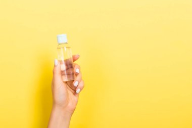 Kadın el tutarak krem şişe losyon izole. Kız sarı arka plan üzerinde kavanoz kozmetik ürünleri vermek
