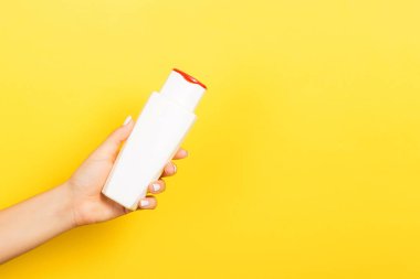 Kadın el tutarak krem şişe losyon izole. Kız sarı arka plan üzerinde tüp kozmetik ürünleri vermek