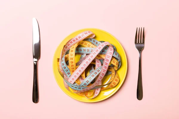 Top view of colorful measuring tapes on plate in the form of spaghetti with knife and fork on pink background. Weight loss and diet concept — Stock Photo, Image