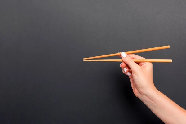 木制筷子在女性手的黑色背景与空白的空间，为您的想法。美味食品概念 — 图库照片
