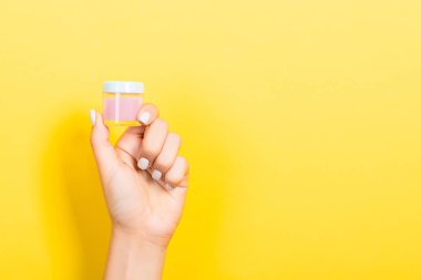 Kadın el tutarak krem şişe losyon izole. Kız sarı arka plan üzerinde kavanoz kozmetik ürünleri vermek