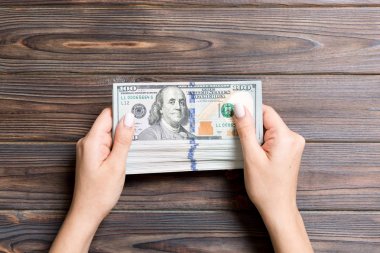 Tahta arka planda 100 dolarlık banknotların kadın ellerinde üst görüntüsü. İş ve mali konsept