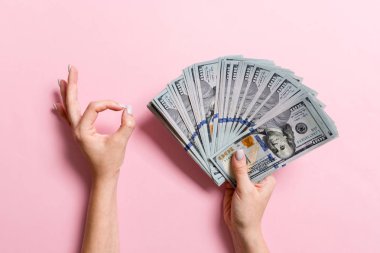 Bir elinde yüz dolarlık banknotların üst görünümü ve renkli arka plan üzerinde başka bir el ile tamam jest gösteren. Refah ve servet kavramı