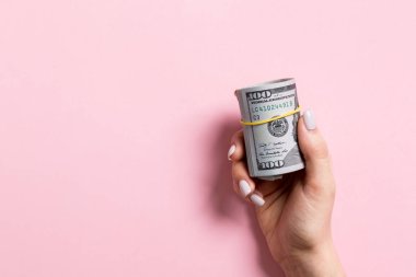 Renkli arka plan üzerinde haddelenmiş para bir paket tutan kadın el üst görünümü. Yüz dolar. Tasarım için boş alan ile Iş konsepti. Sadaka ve ipuçları kavramı