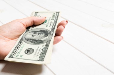 Kadın el ahşap arka plan üzerinde para bir demet tutan. Yüz dolarlık banknotların perspektif görünümü. Tasarım için boş alan ile Maaş kavramı