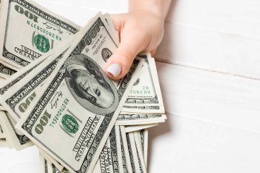 Kadın el ahşap arka plan üzerinde yüz dolarlık banknotlar bir demet tutan. Maaş ve ücret kavramı