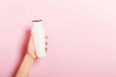 Kadın el tutarak krem şişe losyon izole. Kız pembe arka plan üzerinde tüp kozmetik ürünleri vermek