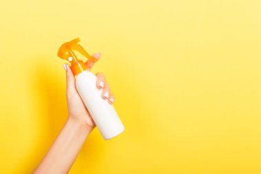 Kadın el losyon izole sprey krem şişe tutarak. Kız sarı arka plan üzerinde kozmetik ürünler vermek