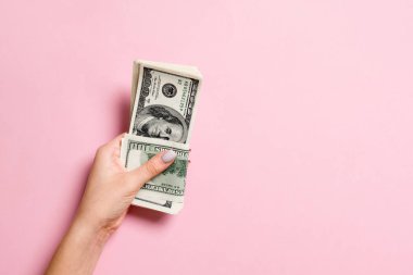 Renkli arka planda yüz dolarlık banknotlar bir paket tutan kadın el üst görünümü. Tasarım için boş alan ile ücret ve maaş kavramı