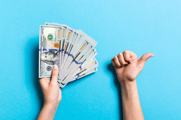 Bir elinde yüz dolarlık banknotların üst görünümü ve renkli arka plan üzerinde başka bir el ile başparmak kadar jest gösteren. Refah ve servet kavramı