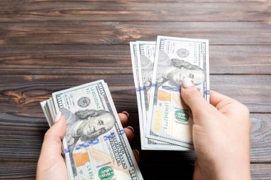 Kadın el ahşap arka plan üzerinde yüz dolarlık banknotlar veriyor. Zenginlik kavramına bakış açısı
