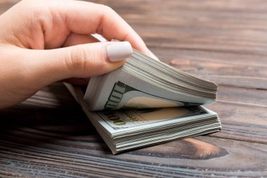 Ahşap arka planda yüz dolarlık banknotlar sayan bir iş kadınının ellerine bakış açısı. Başarı ve zenginlik kavramı