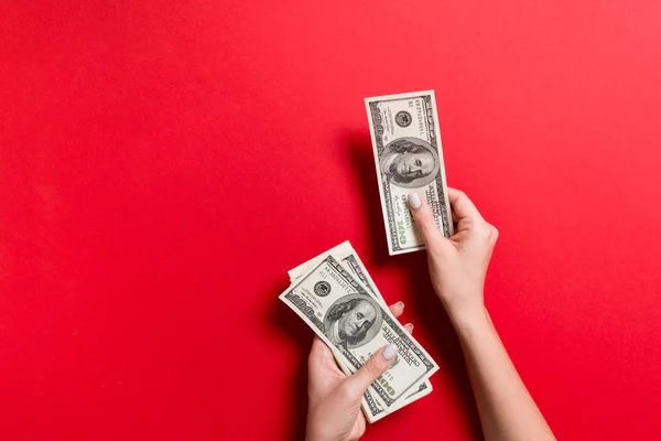 Mano femenina dando billetes de cien dólares sobre fondo colorido. Vista superior del concepto de riqueza con espacio vacío para su diseño — Foto de Stock