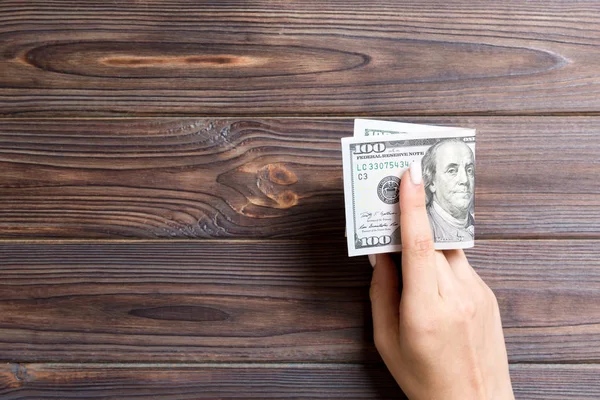 Balík 100 dolarových bankovek v rukou na dřevěném pozadí. Koncept mezd s prostorem pro kopírování — Stock fotografie