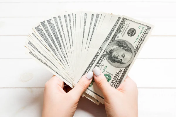 Perspectiva de la mano femenina sosteniendo un ventilador de dinero sobre fondo de madera. Billetes de cien dólares. Concepto de crédito y deuda — Foto de Stock