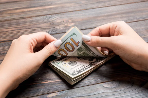 Vista prospettica delle mani di una donna d'affari che conta banconote da cinque e cento dollari su sfondo di legno. Concetto di successo e ricchezza — Foto Stock