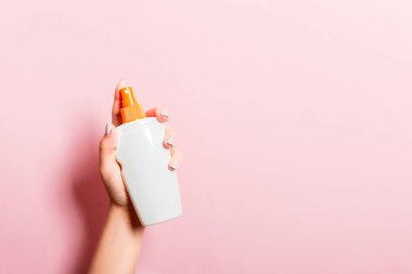 Kadın el losyon izole sprey krem şişe tutarak. Kız pembe arka plan üzerinde kozmetik ürünler vermek