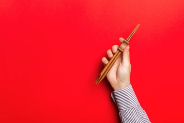 Kırmızı arka planda yemek çubuğu tutan erkek eli görüntüsü. Kopya alanı olan Asya yemekleri konsepti