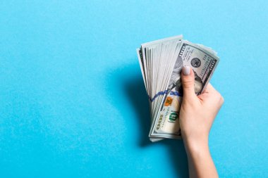 Renkli arka planda yüz dolarlık banknotlar bir paket tutan kadın el üst görünümü. Tasarım için boş alan ile ücret ve maaş kavramı