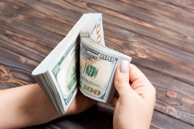 Ahşap arka planda yüz dolarlık banknotlar sayan bir iş kadınının ellerine bakış açısı. Başarı ve zenginlik kavramı