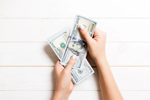 Mano femenina dando billetes de cien dólares sobre fondo de madera. Vista superior del concepto de riqueza — Foto de Stock