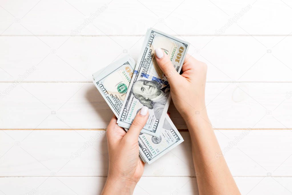 Female hand giving one hundred dollar banknotes on wooden background. Top view of wealth concept