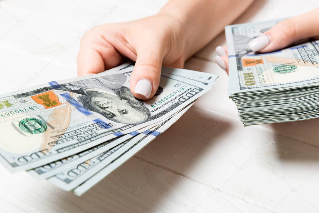 Female hand giving one hundred dollar banknotes on wooden background. Perspective view of wealth concept
