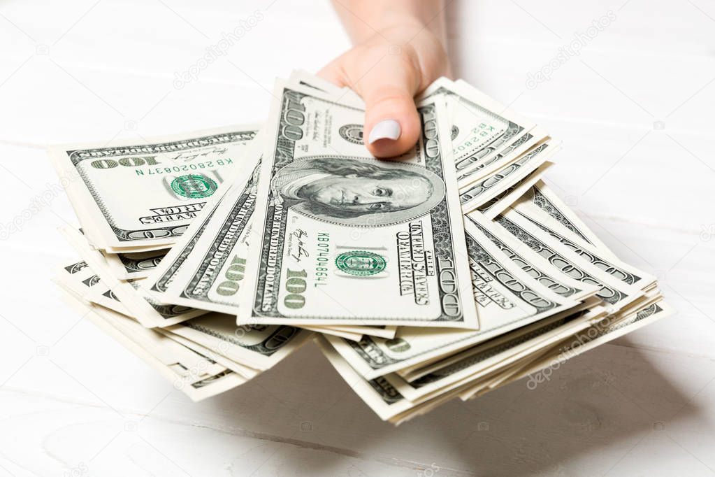 Female hand holding a bundle of one hundred dollar banknotes on wooden background. Salary and wage concept