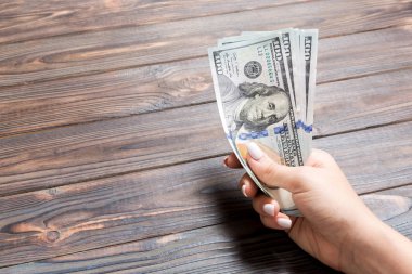 Kadın el ahşap arka plan üzerinde yüz dolarlık banknotlar bir demet tutan. Fotokopi alanı ile maaş ve ücret kavramı
