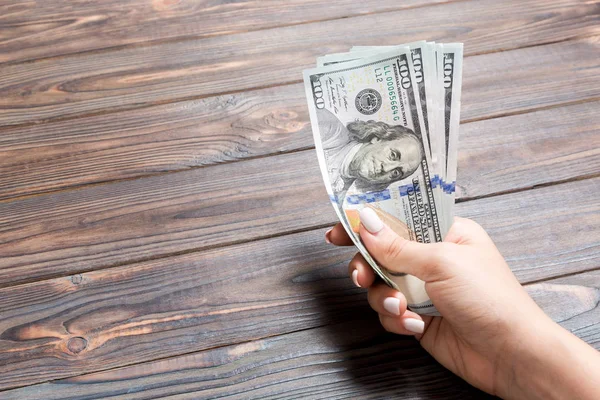 Samičí ruka držící svazek 100 dolarových bankovek na dřevěném pozadí. Koncepce mezd a mezd s prostorem pro kopírování — Stock fotografie