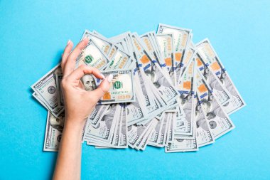 Bir elinde yüz dolarlık banknotların üst görünümü ve renkli arka plan üzerinde başka bir el ile tamam jest gösteren. Refah ve servet kavramı