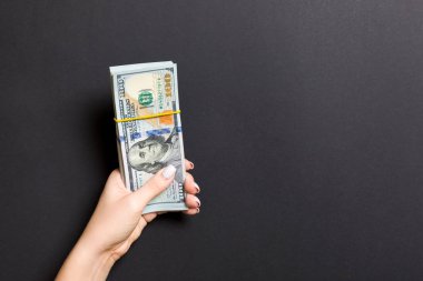 Renkli arka planda yüz dolarlık banknotlar bir paket tutan kadın el üst görünümü. Tasarım için boş alan ile ücret ve maaş kavramı