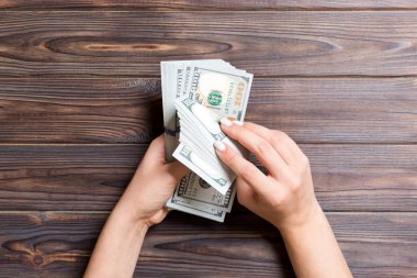 Ahşap arka plan üzerinde yüz dolarlık banknotlar sayan bir iş kadınının ellerinin üst görünümü. Başarı ve zenginlik kavramı