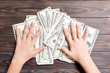 Yüz dolarlık banknotların üzerinde uzanan kadın eli manzarası. Tahta arka planda başarı ve zenginlik kavramı
