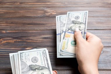 Kadın el ahşap arka plan üzerinde yüz dolarlık banknotlar veriyor. Zenginlik kavramına bakış açısı