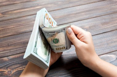 Ahşap arka planda yüz dolarlık banknotlar sayan bir iş kadınının ellerine bakış açısı. Başarı ve zenginlik kavramı