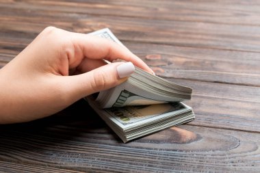 Ahşap arka planda yüz dolarlık banknotlar sayan bir iş kadınının ellerine bakış açısı. Başarı ve zenginlik kavramı