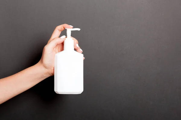 Mão feminina segurando spray creme garrafa de loção isolada. Menina dar produtos cosméticos em blakbackground — Fotografia de Stock