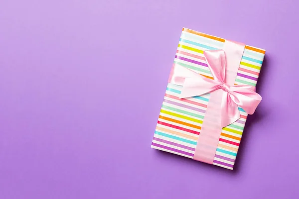 Top vista donna mani in possesso di regalo di Natale scatola con fiocco rosa su sfondo viola con spazio copia — Foto Stock