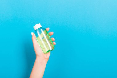 Kadın el tutarak krem şişe losyon izole. Kız mavi arka plan üzerinde tüp kozmetik ürünleri vermek