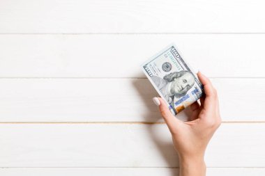 Ahşap arka planda kadın elinde yüz dolarlık banknotlar bir paket. Kopya alanı ile maaş kavramı
