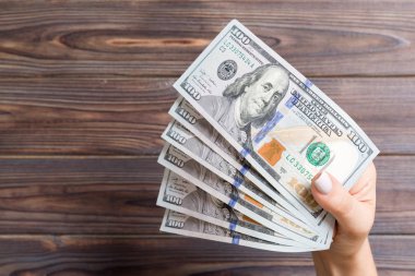 Kadın eli ahşap arka planda bir para yelpazesini tutuyor. Yüz dolarlık banknotlar. Kredi ve borç kavramı